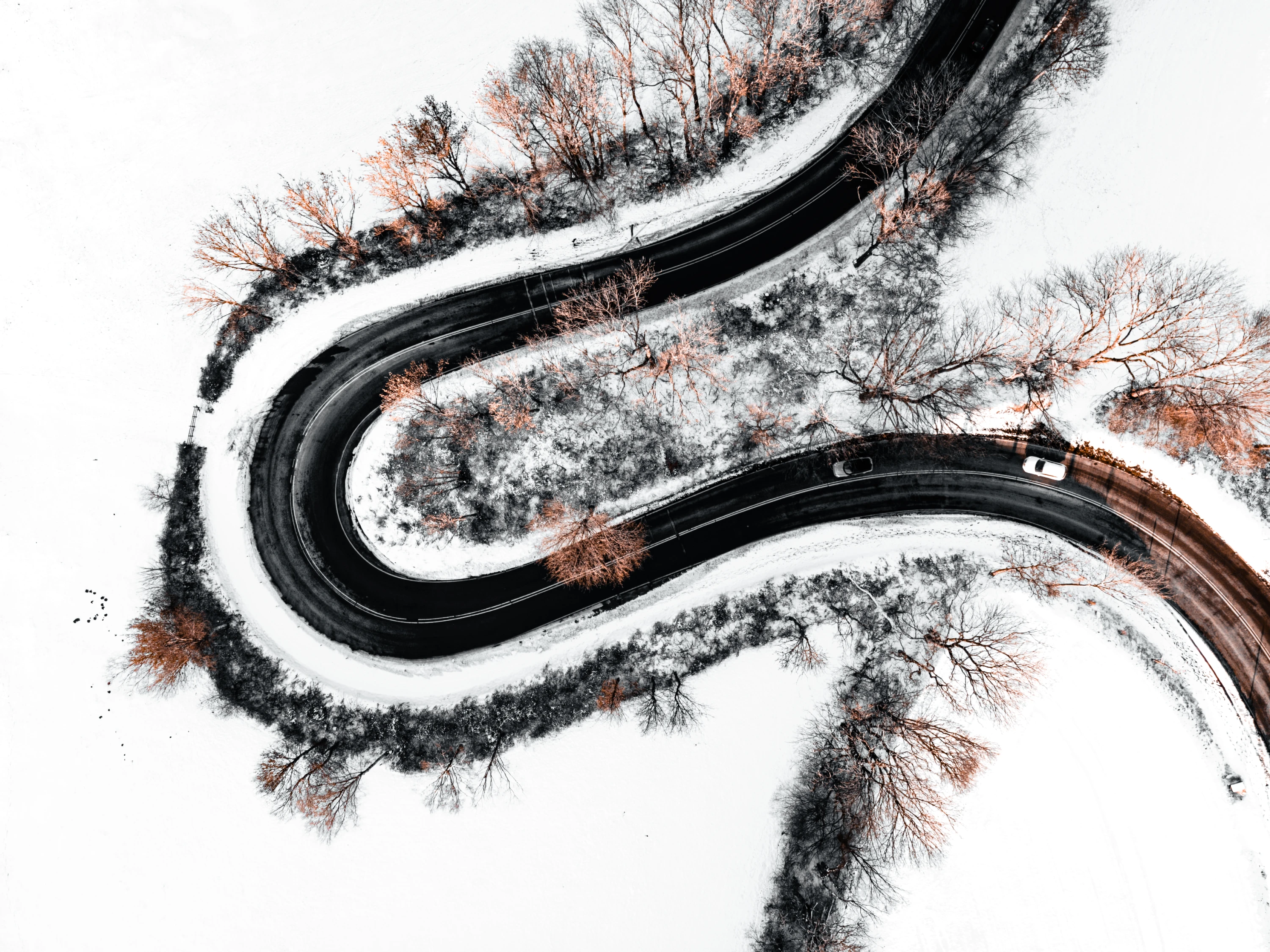 Luftaufnahme einer verschneiten, kurvigen Straße mit Herbstlaub